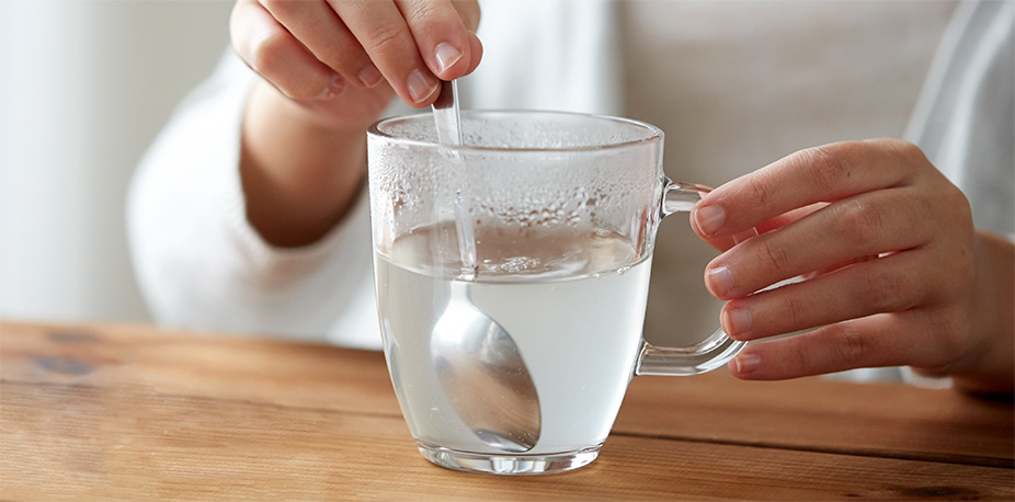 A woman stirs a glass of water with OTC IBS-C or CIC medication. 
